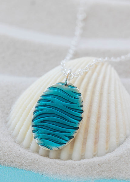 Silver Oval Blue Ripple pendant resting on white shall by Kate Wimbush Jewellery