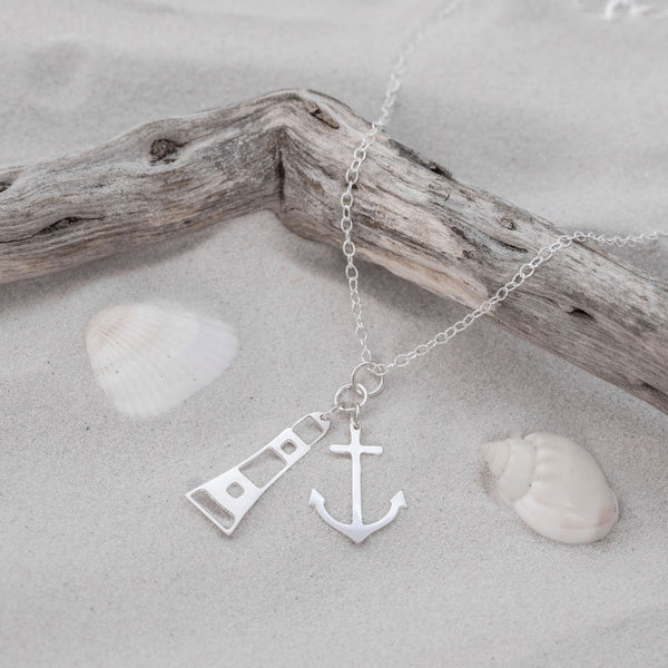 Silver Lighthouse and Anchor Charm Pendant on sand and driftwood, by Kate Wimbush Jewellery