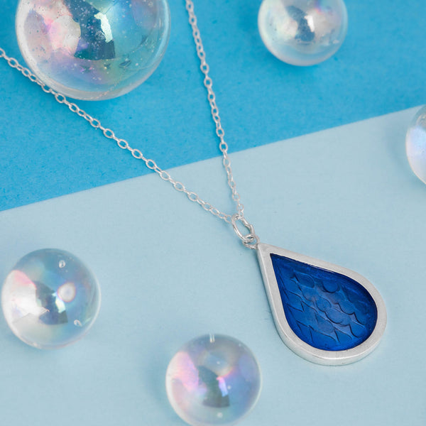 Silver Blue Stamped Raindrop Pendant, weather jewellery on blue background, by Kate Wimbush Jewellery