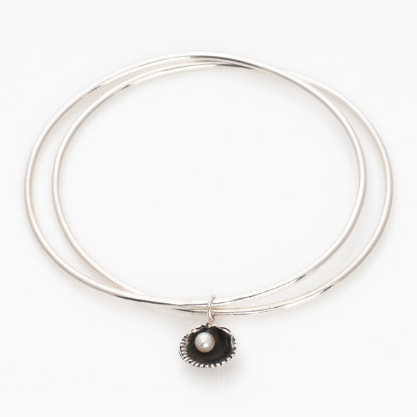 Silver double bangle with oxidised cockle shell charm and white freshwater pearl on white background by Kate Wimbush Jewellery