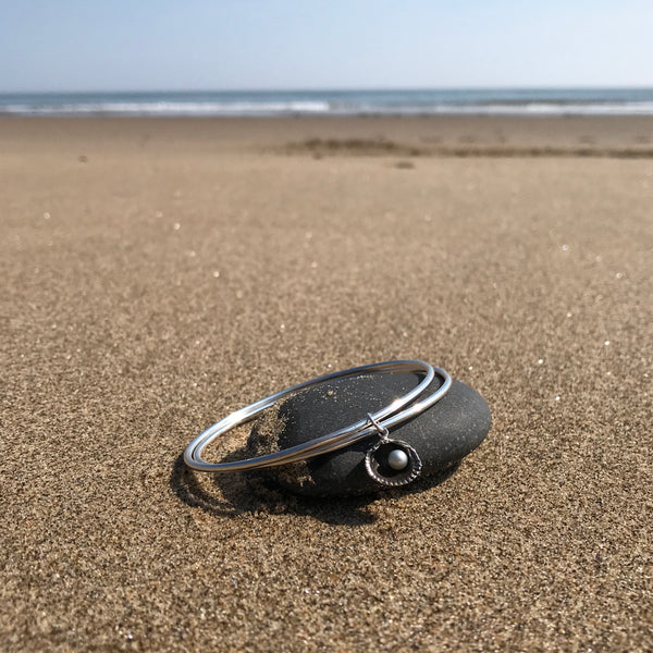 Silver double bangle with small cockle shell charm on Scarborough beach by Kate Wimbush Jewellery